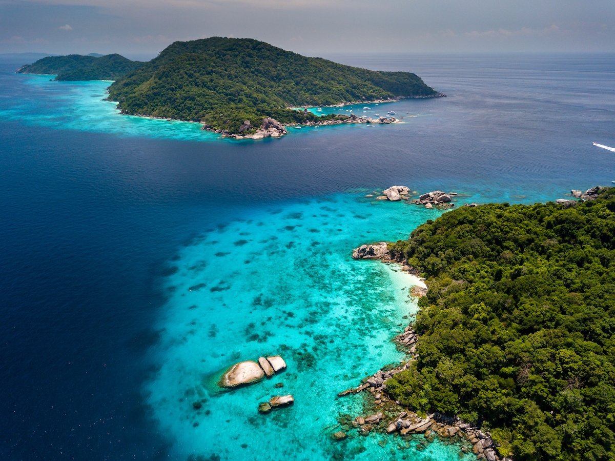 Aerial view of a deserted, jungle covered tropical island with crystal clear ocean below (c) 