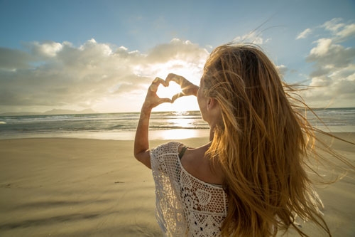 Woman-on-beach-makes-heart-shape-finger-frame-to-sunset-576906184_5760x3840_LQ_swissmediavision (c) ©istock/swissmediavision